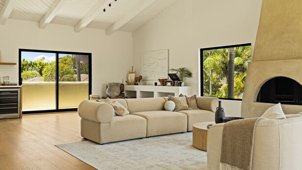 Ein modernes Wohnzimmer mit einem Ecksofa, einem Kamin und großen Fenstern mit Blick auf Grünflächen.
