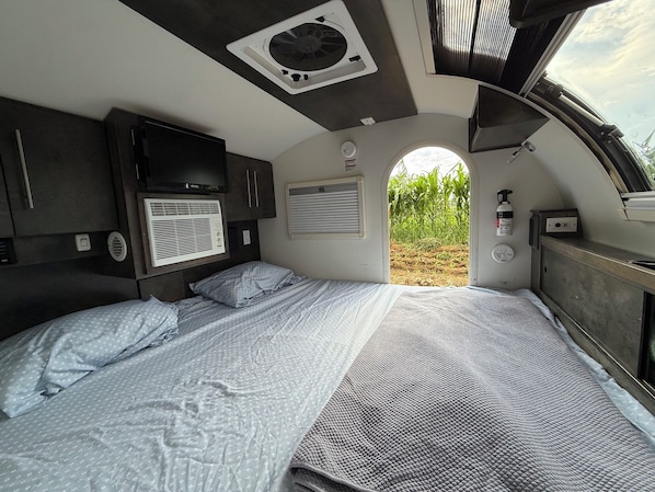 A compact RV bedroom with a bed, a ceiling fan, a window, and a view of the outdoors. - Teardrop trailer on a working farm outside Oaxaca City. (San Lorenzo Cacaotepec)