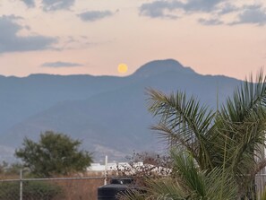 A mountain landscape with a sun in the sky, palm trees, and a water tank. - Teardrop trailer on a working farm outside Oaxaca City. (San Lorenzo Cacaotepec)
