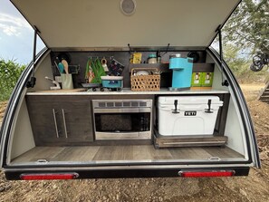 A compact kitchen with a microwave, stove, and storage box labeled 'YETI'. - Teardrop trailer on a working farm outside Oaxaca City. (San Lorenzo Cacaotepec)