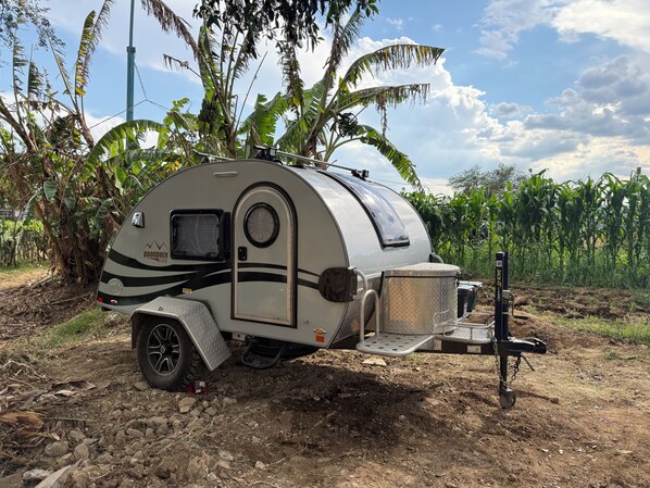 A compact recreational vehicle parked in a rural area with a trailer attached.