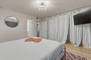 A bedroom with a bed, a flat-screen TV, a mirror, and white curtains. - Gated Austin 2BR Condo+ Pool - Near South Congress (Austin)