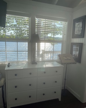 Una habitación con un aparador blanco, una lámpara y una ventana con persianas.