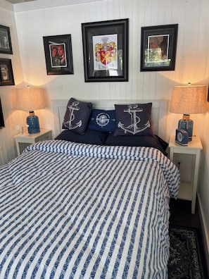 A bedroom with a striped bedspread, framed pictures on the wall, and matching nightstands with lamps.