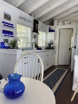 A kitchen with white cabinets, a blue vase on the table, and a patterned rug. - COZY 1-bedroom Charming Cottage located in Midcoast Maine 15 minutes from Camden (Appleton)