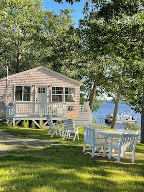 A lakeside cabin with a deck, outdoor seating, and a boat docked nearby.