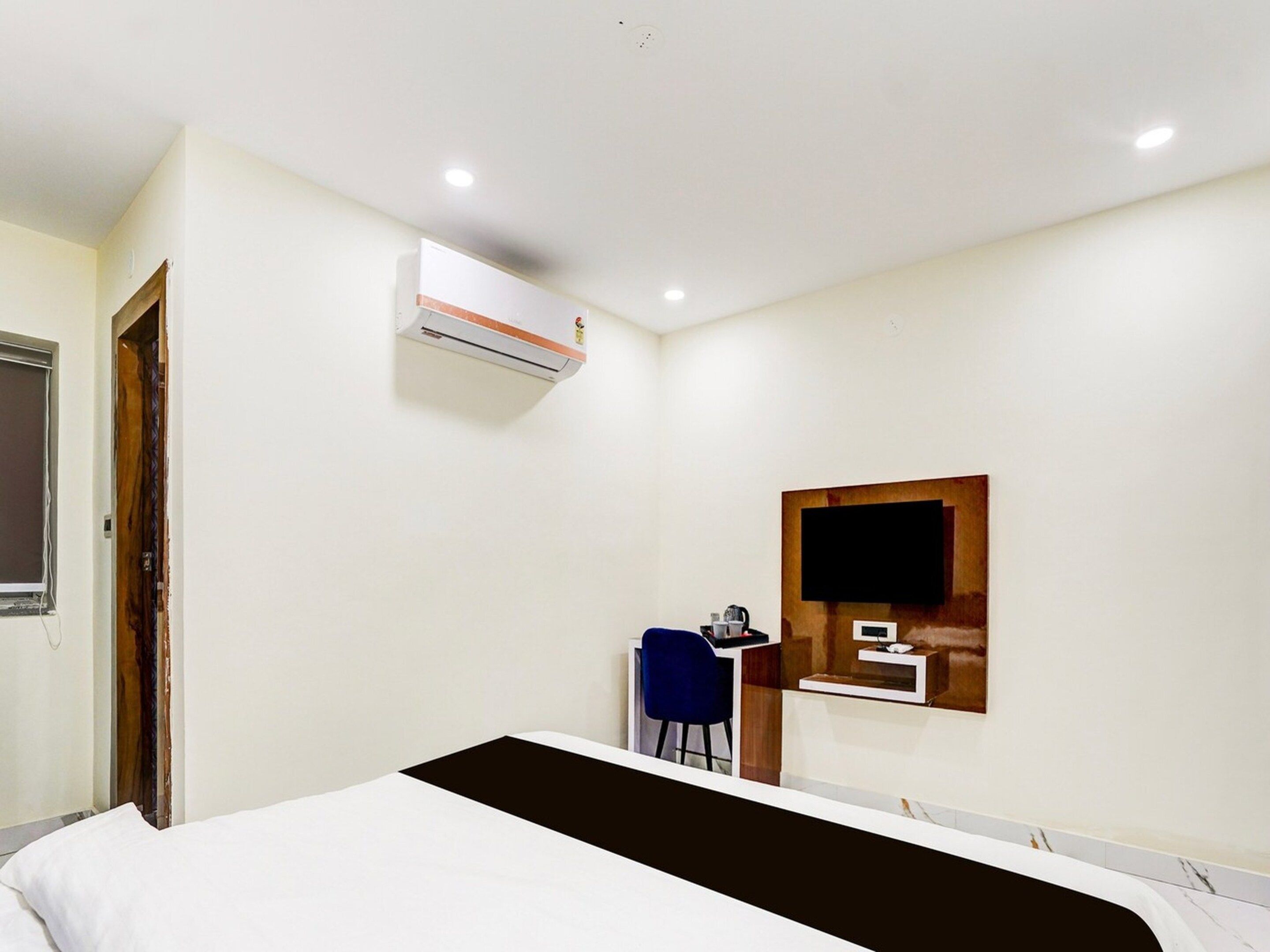 A hotel room with a bed, a desk, a chair, an air conditioning unit, and a television mounted on the wall.