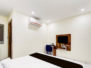 A hotel room with a bed, a desk, a chair, an air conditioning unit, and a television mounted on the wall.