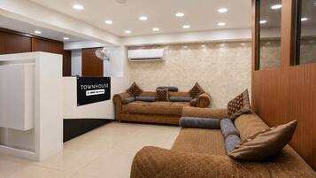 A modern living area with a sofa set, a white reception desk, and an air conditioning unit on the wall.