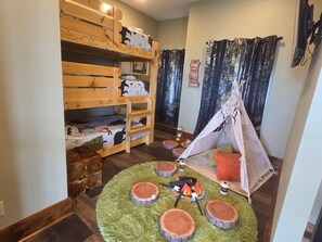 Ein Zimmer mit Etagenbetten, einem Zelt und einem Rundteppich mit Baumstamm-Motiven.