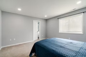 Un dormitorio con una cama individual, una puerta que da a un baño y una ventana con persianas.