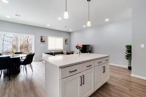 Cozinha moderna com ilha central, iluminação pendente e área de jantar com mesa e cadeiras.