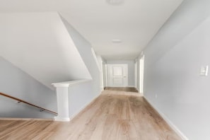 Un pasillo con piso de madera, paredes blancas y una puerta blanca al final.