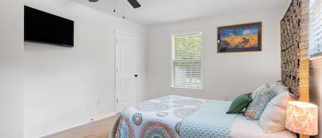 Un dormitorio con una cama, un ventilador de techo, una ventana con persianas, un cuadro y una lámpara.