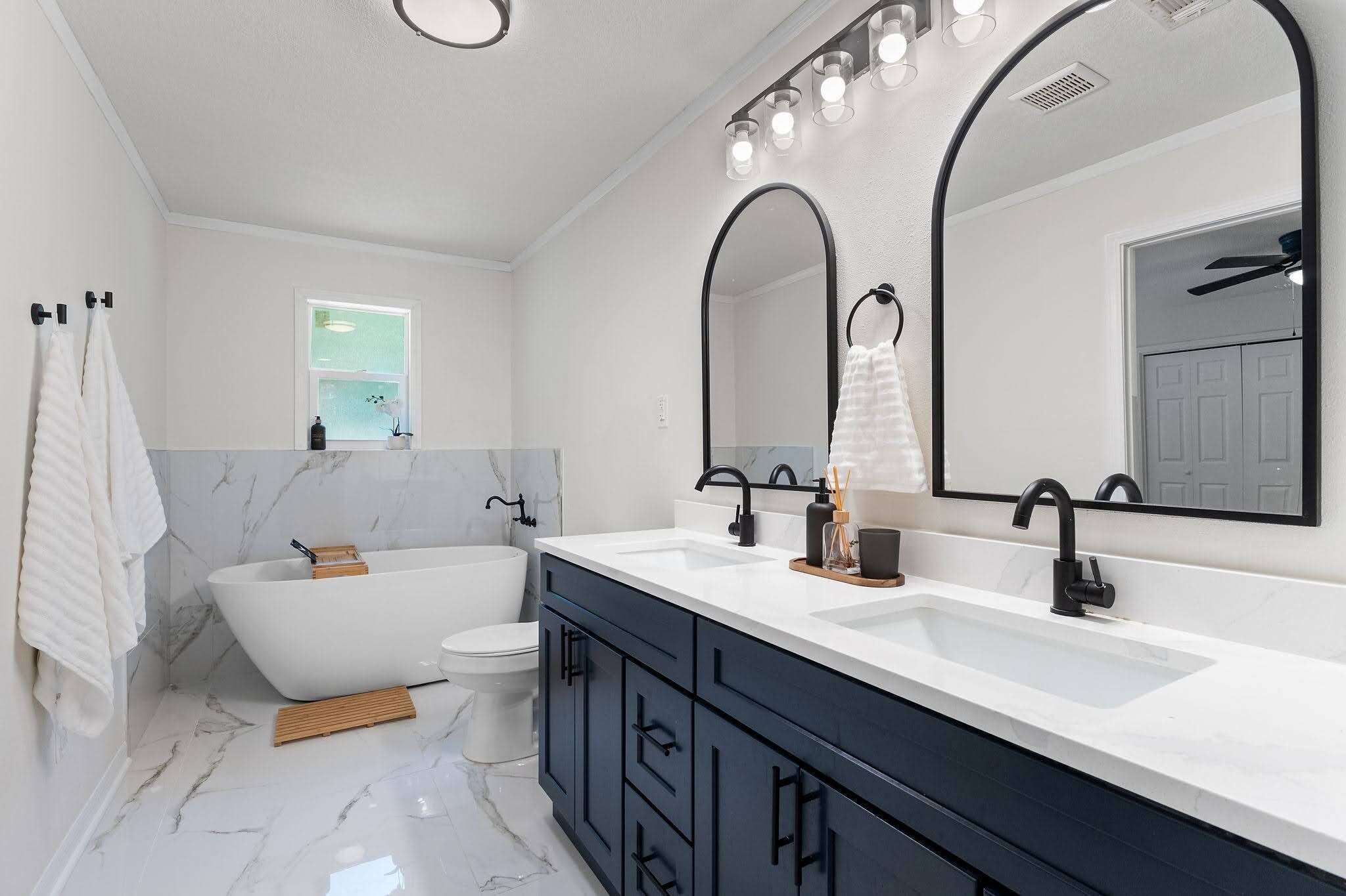 Step into your spa-like ensuite with dual vanities, elegant oval mirrors, and a luxurious soaking tub framed by marble. Fresh towels and warm natural light make this your perfect retreat.