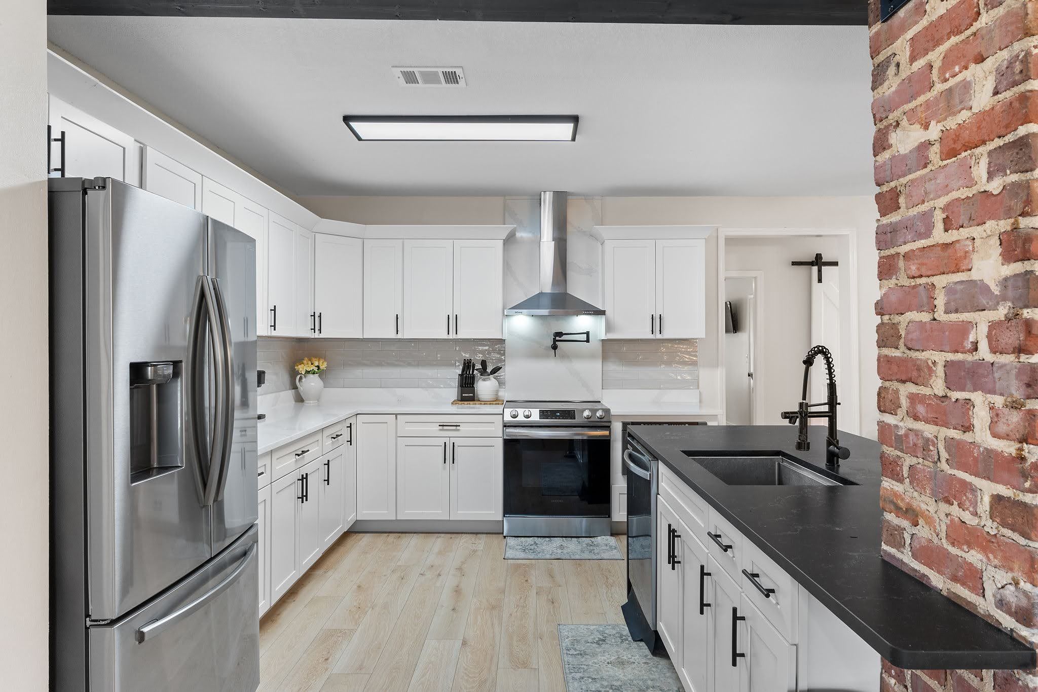 Een moderne keuken met witte kasten, roestvrijstalen apparatuur en een accentmuur van baksteen.