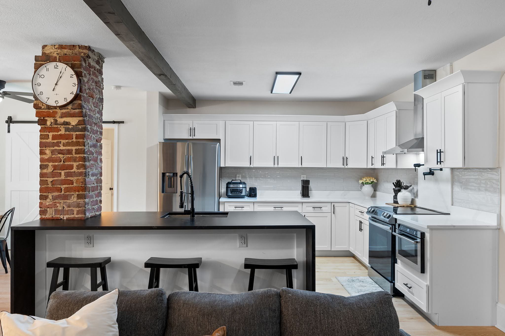A modern kitchen with white cabinets, a brick column, stainless steel appliances, and a bar area with stools.