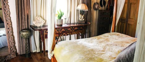 A bedroom with a large bed, a wooden dresser, a desk with a lamp, and a mirror.