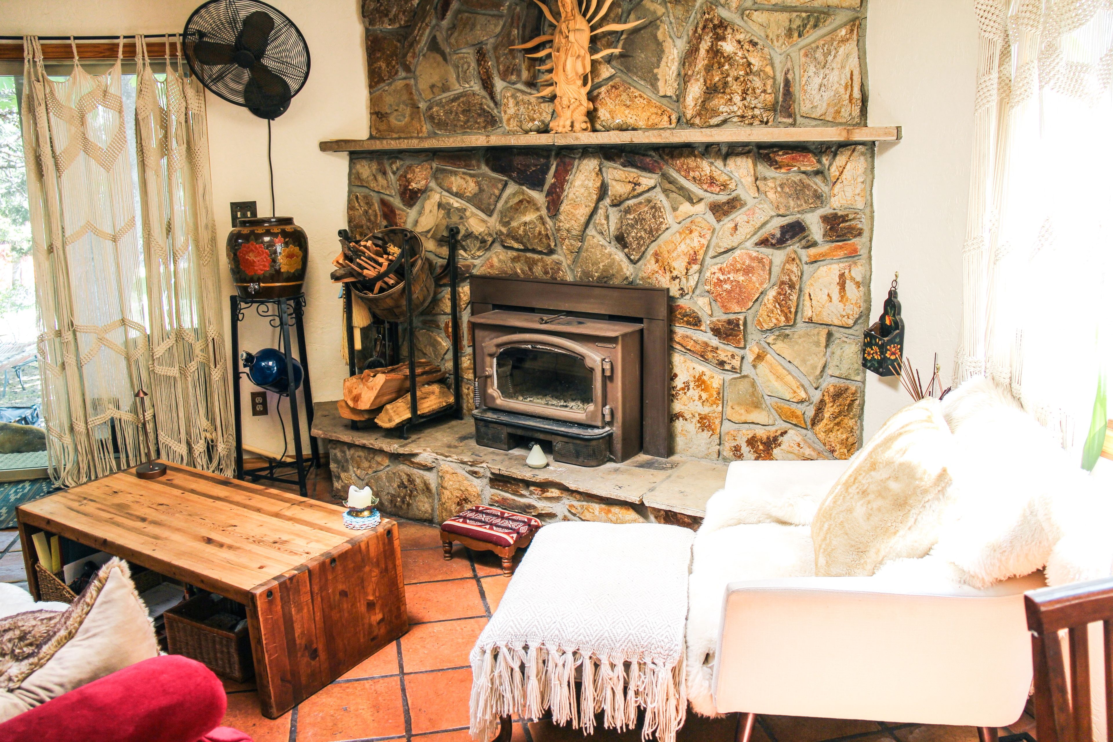 Een gezellige woonkamer met een stenen openhaard, houten meubels en een ventilator.