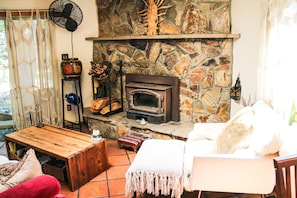 Ein gemütliches Wohnzimmer mit Kamin aus Stein, Holzmöbeln und einem Ventilator.