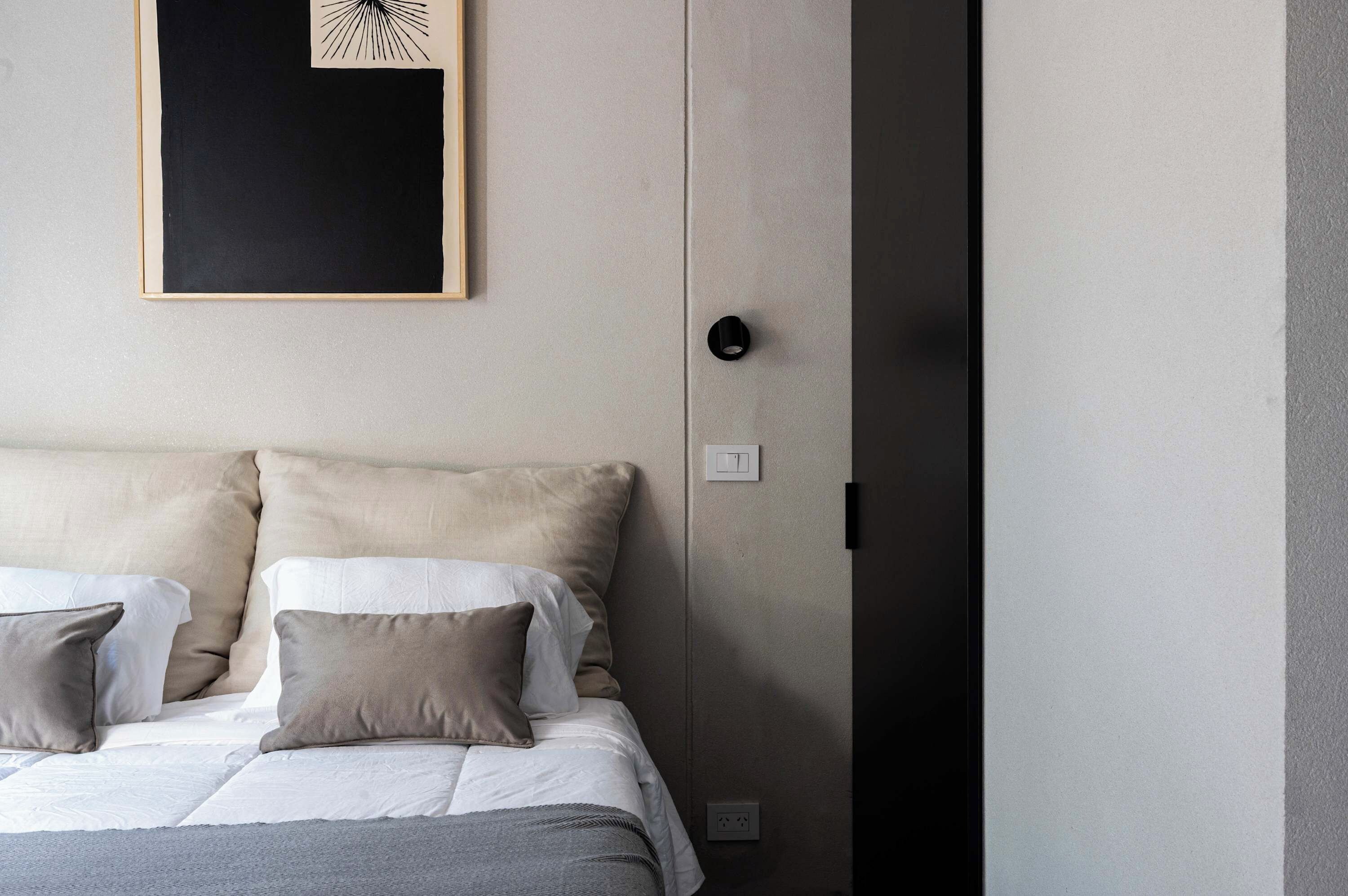 A neatly made bed with two pillows and a blanket, a wall-mounted light switch, and a power outlet.
