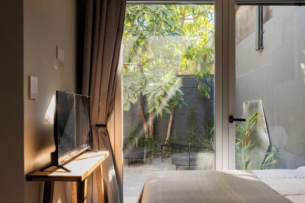 A bedroom with a bed, a desk, and a view of a garden through a glass door.