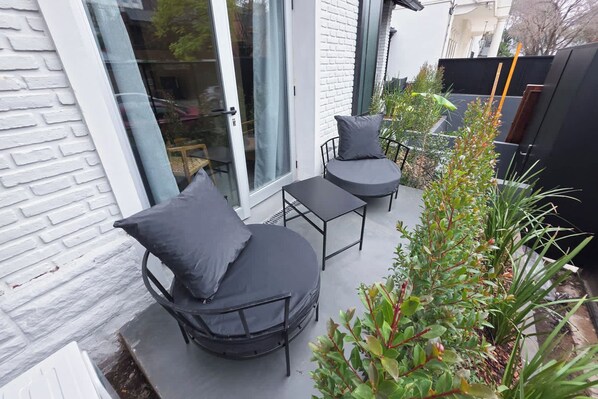 An outdoor seating area with a table and two chairs, a glass door, and a white brick wall.