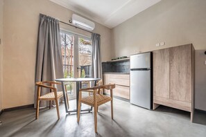 Eine kleine Küche mit Kühlschrank, einem Esstisch mit Stühlen und einem Fenster mit Vorhängen.