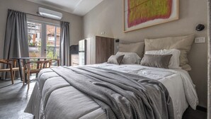 A hotel room with a bed, a desk, and a chair. There is a window with curtains, a wall-mounted air conditioner, and a painting on the wall. - MOT Rentals River Plate Loft 1 - 100m to Stadium (Buenos Aires)