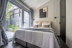A bedroom with a bed, a sliding glass door to a balcony, and a wall-mounted artwork.