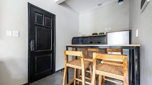 Eine kompakte Küche mit einer schwarzen Tür, einem kleinen Essbereich mit zwei Holzkohle und einem weißen Kühlschrank.