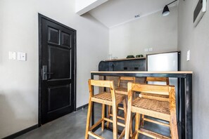 Eine kompakte Küche mit einer schwarzen Tür, einem kleinen Essbereich mit zwei Holzkohle und einem weißen Kühlschrank.