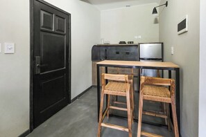 A compact kitchen with a black door, a small dining table with two wooden chairs, a refrigerator, and a television.