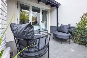 A patio with two chairs and a table, a glass door, and a small plant.