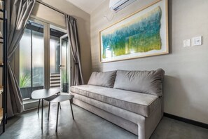 Ein modernes Wohnzimmer mit einem grauen Sofa, einem kleinen Tisch und einem großen abstrakten Gemälde an der Wand.