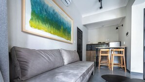 Ein modernes Wohnzimmer mit einem grauen Sofa, einem schwarzen Couchtisch und einem großen abstrakten Gemälde an der Wand.