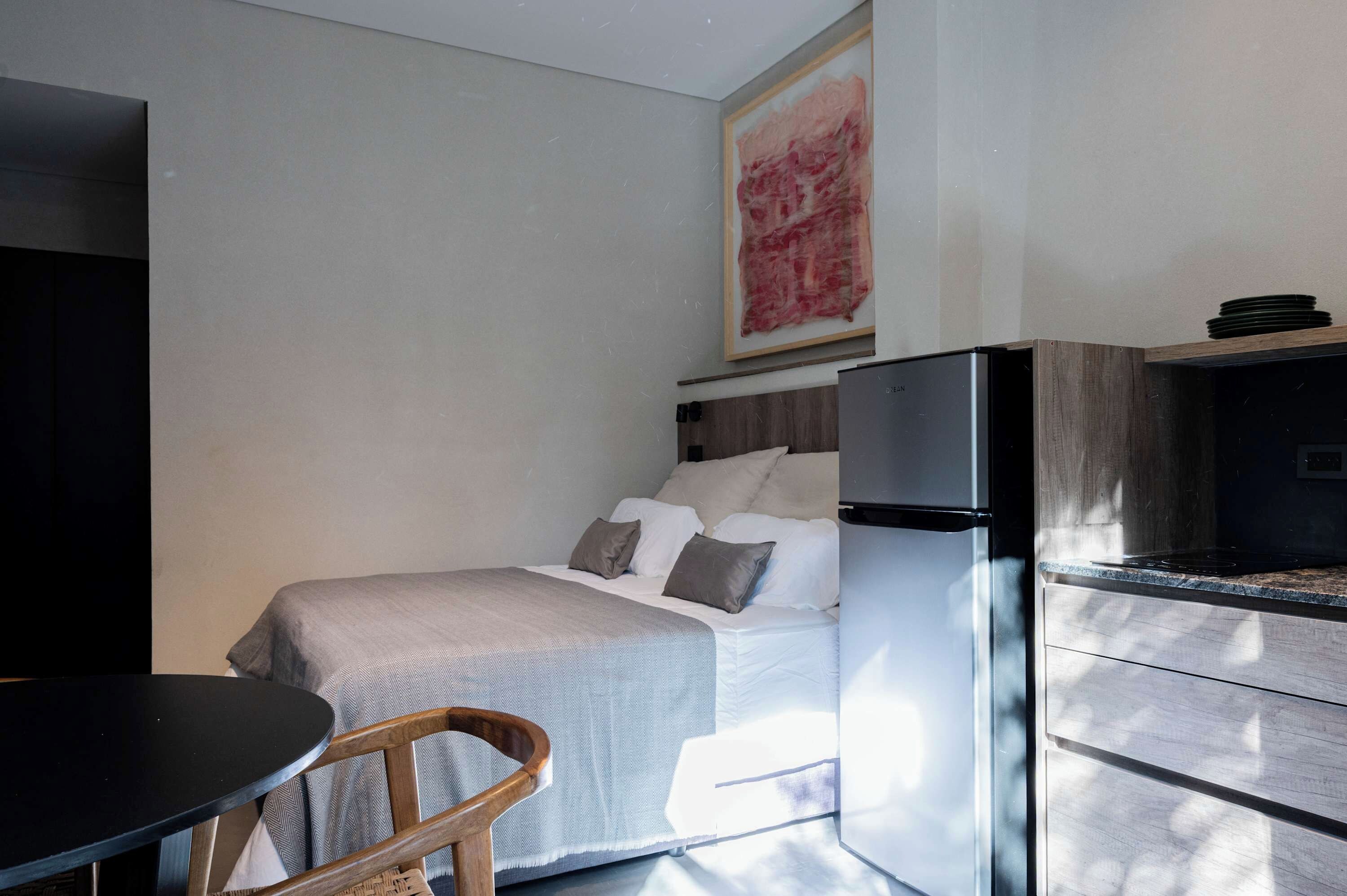 A modern bedroom with a bed, a small table, and a built-in kitchen area.