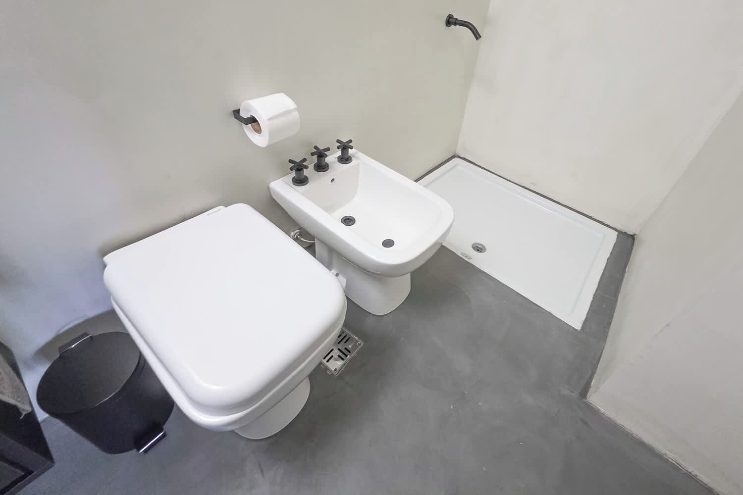 A small bathroom with a toilet, bidet, and a trash bin.
