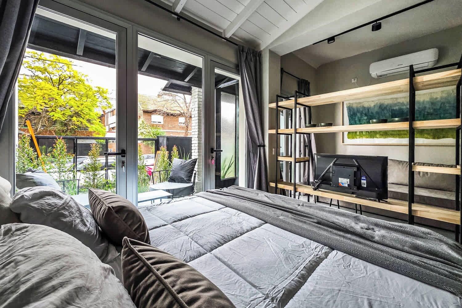 A modern bedroom with a large bed, a desk with a computer, and a view of the outside.