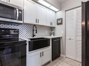 Une cuisine avec des meubles blancs, un four à micro-ondes, une cuisinière, un lave-vaisselle et un réfrigérateur.