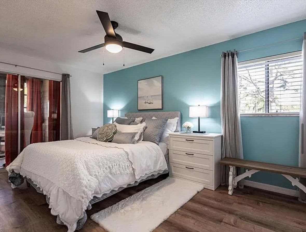 Une chambre à coucher avec un lit, des tables de chevet, un ventilateur de plafond et une fenêtre avec des rideaux.