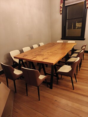 Uma sala de conferência com mesa de madeira rodeada por cadeiras, uma janela com vista e uma parede simples.