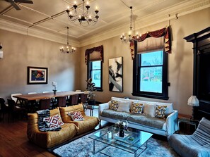 Uma sala de estar com sofá, poltronas, mesa de centro e um espaço de jantar com mesa e cadeiras.