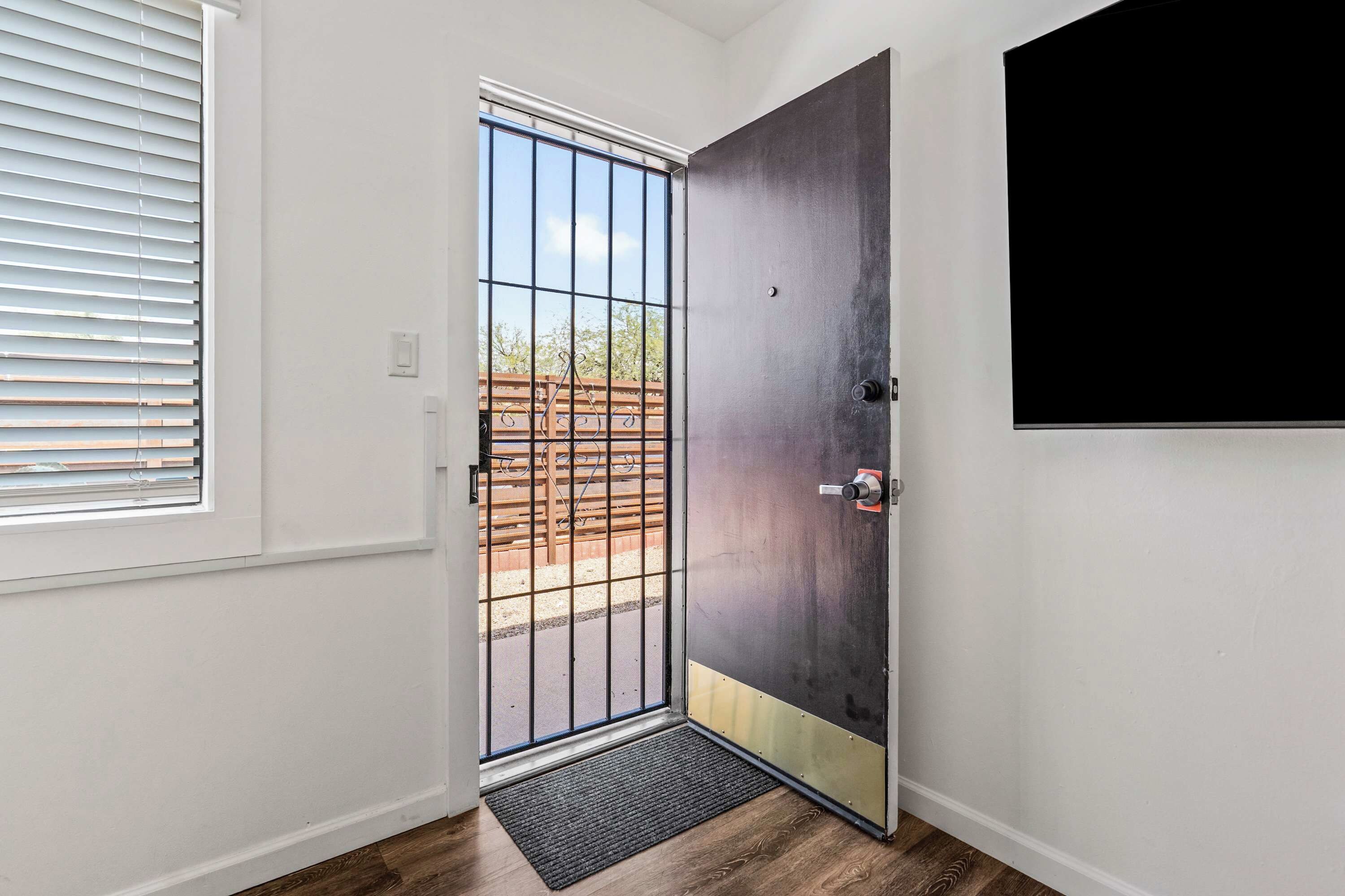 A room with a door leading to an outdoor area, a window with blinds, and a wall-mounted television.