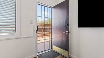 A room with a door leading to an outdoor area, a window with blinds, and a wall-mounted television.