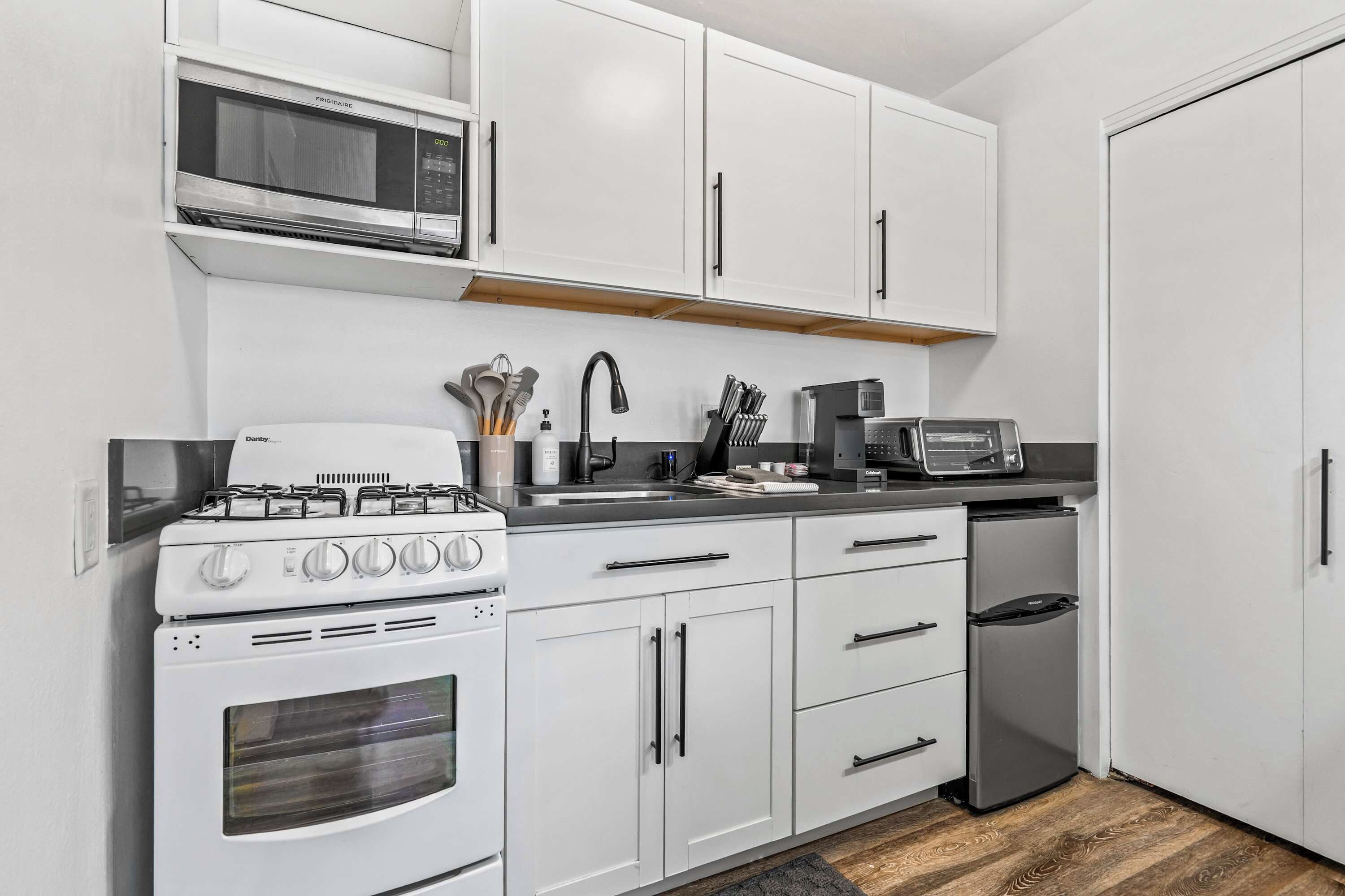 A compact kitchen with white cabinetry, a gas stove, a microwave, and a built-in oven.
