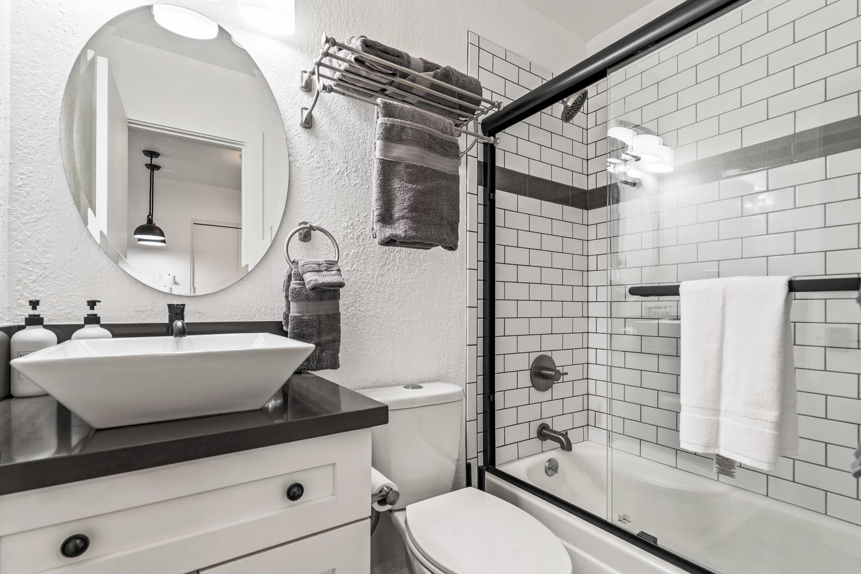 Un baño moderno con lavamanos blanco, un espejo, inodoro y cabina de ducha con mampara de vidrio.