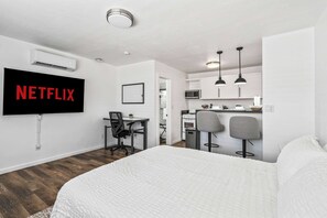 Ein modernes Hotelzimmer mit einem Bett, einem Schreibtisch, einem Sessel, einem an der Wand montierten Fernseher und einer Küchenzeile.