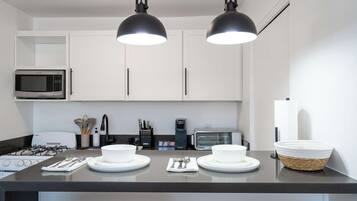 A modern kitchen with white cabinets, a microwave, a toaster, and a gas stove. There are two pendant lights above the counter.