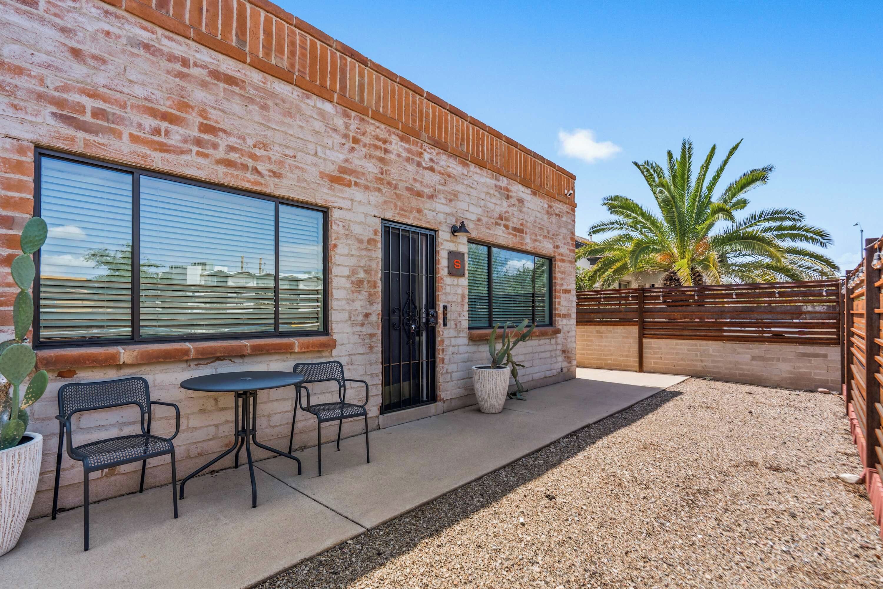 A building with a brick facade, large windows, and a patio area with outdoor seating.